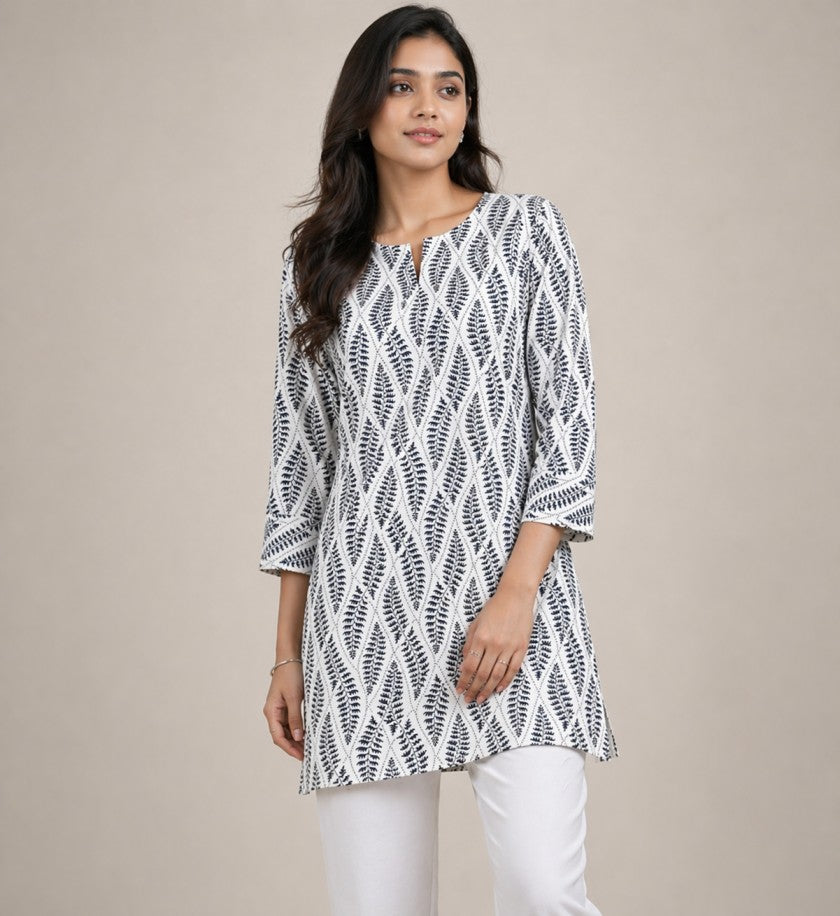 Woman wearing a black and white patterned tunic with white pants on a beige background
