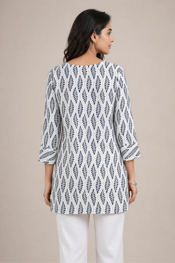 Woman wearing a white and black patterned top with white pants on a beige background
