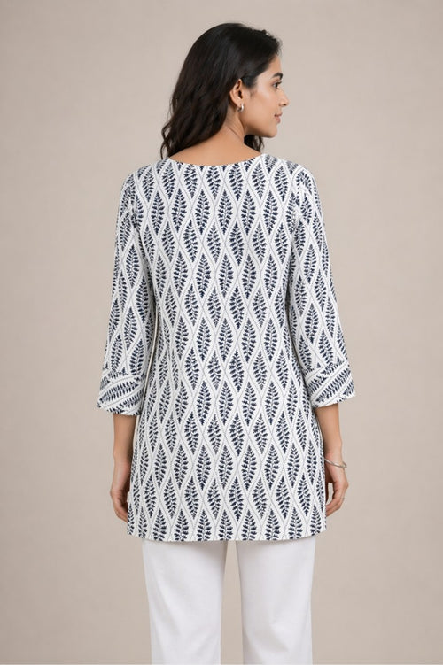 Woman wearing a white and black patterned top with white pants on a beige background