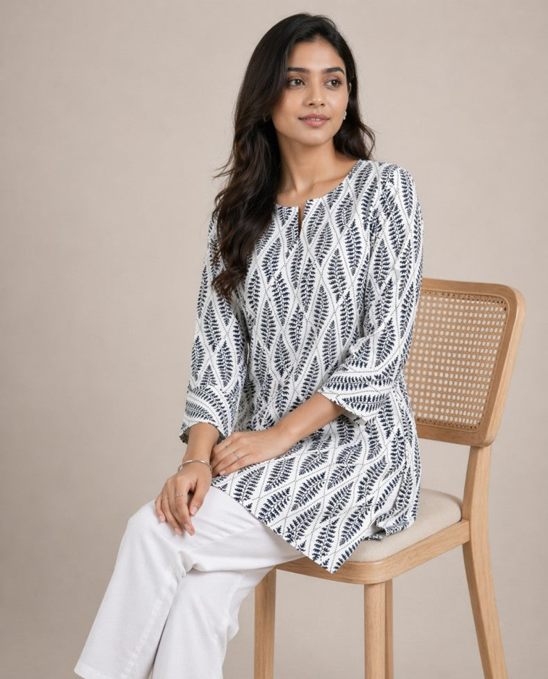 Woman sitting on a chair wearing a black and white patterned dress against a beige background