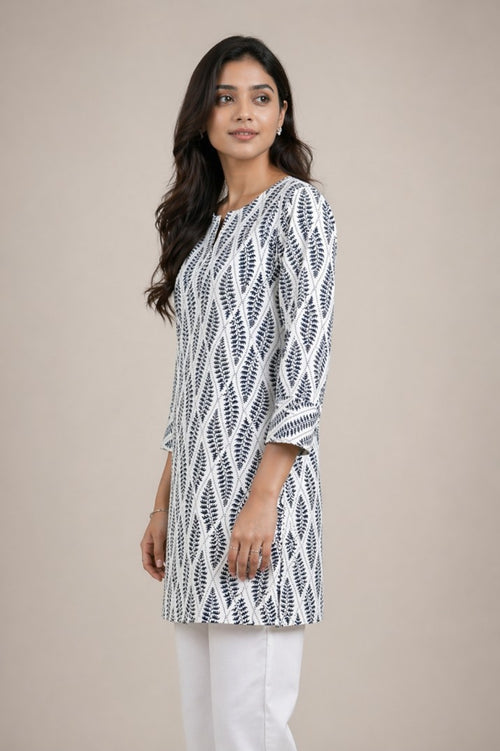Woman wearing a black and white patterned kurta with white pants on a beige background